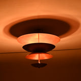 Side view of the illuminated layered brass flushmount chandelier showing soft ambient glow from its concentric copper-finish bowl shades.