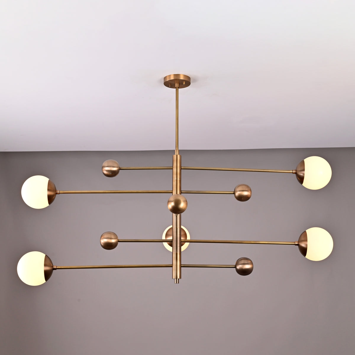 Top-angle view of linear 5-light brass chandelier featuring spherical opal globes arranged on geometric brass rods.