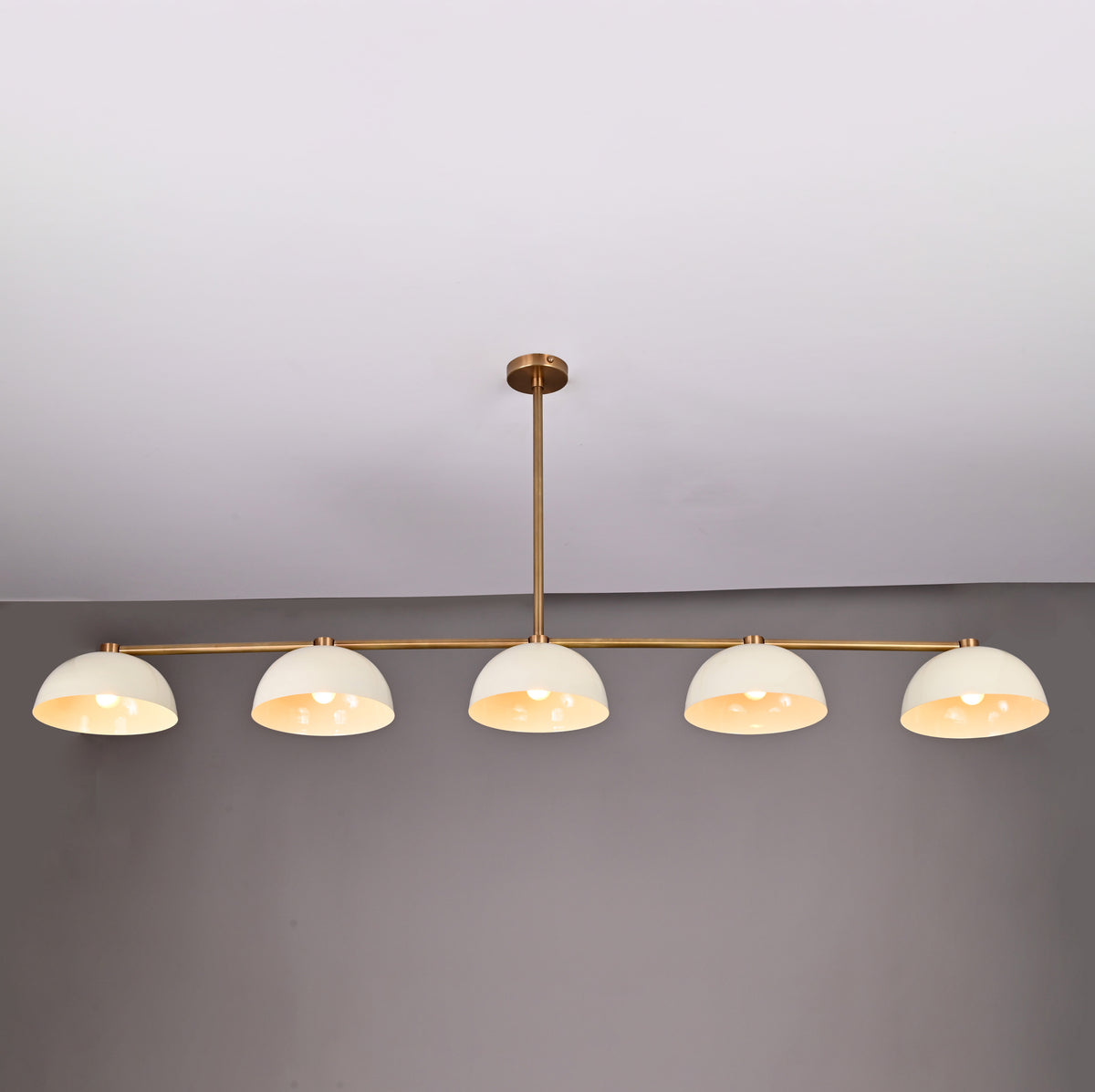 Full front view of 5-light linear brass chandelier with enamel dome shades and downrod ceiling mount in neutral interior
