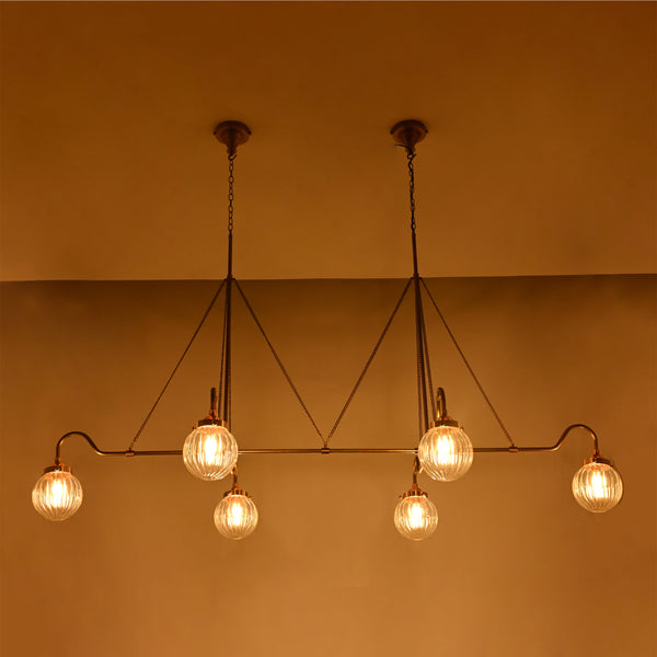 Linear 6-light ribbed glass globe chandelier shown in a warm bedroom interior with brass frame and ambient ceiling lighting