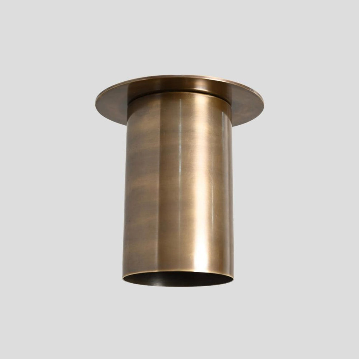 Angled view of elongated brass cylinder flush mount ceiling lamp with lacquer-coated finish