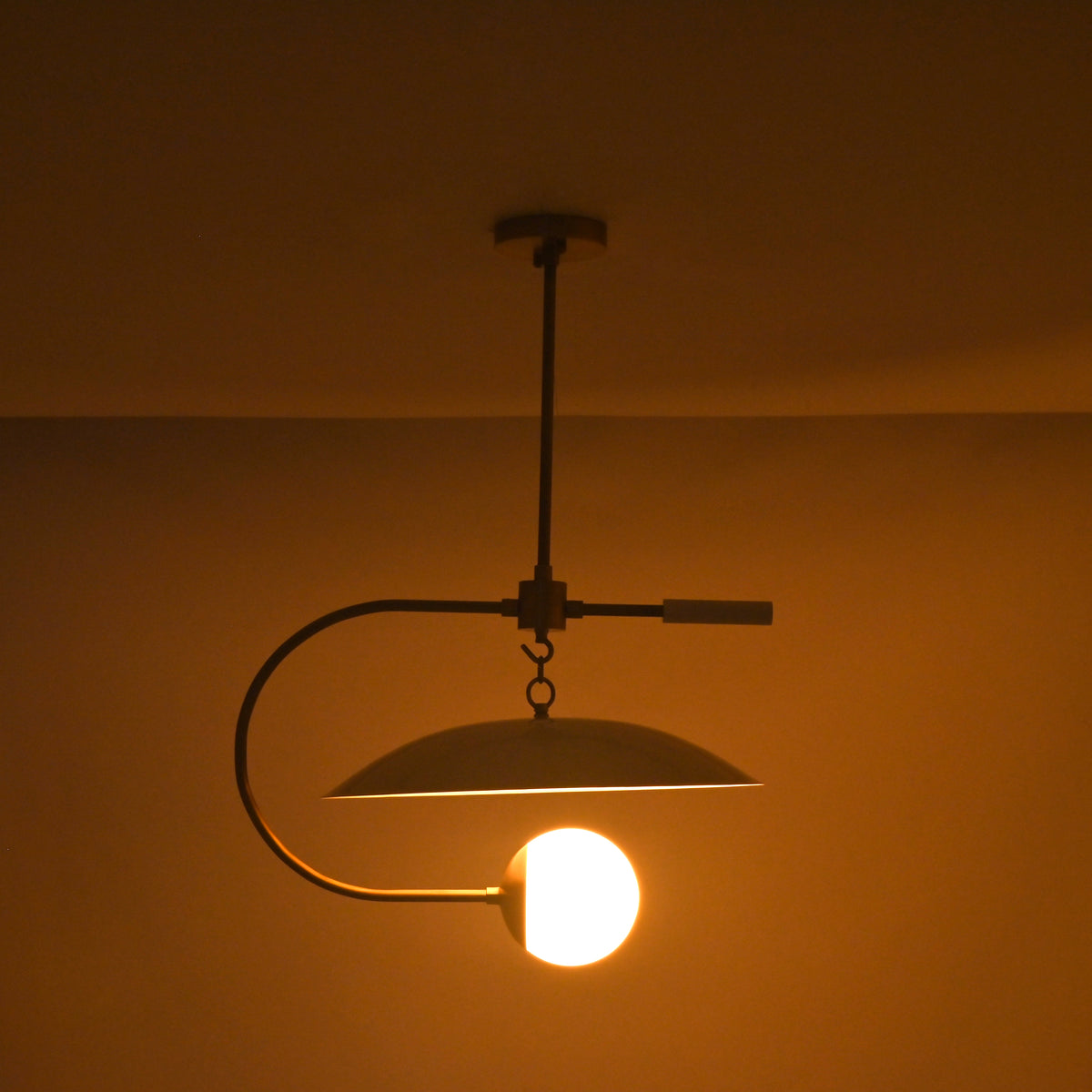 Mid century saucer pendant light with asymmetrical curved arm and frosted globe diffuser design
