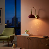 Mallorca brass wall sconce with red enamel bowl shade, curved brass arm, and warm downward glow for bedroom or hallway lighting