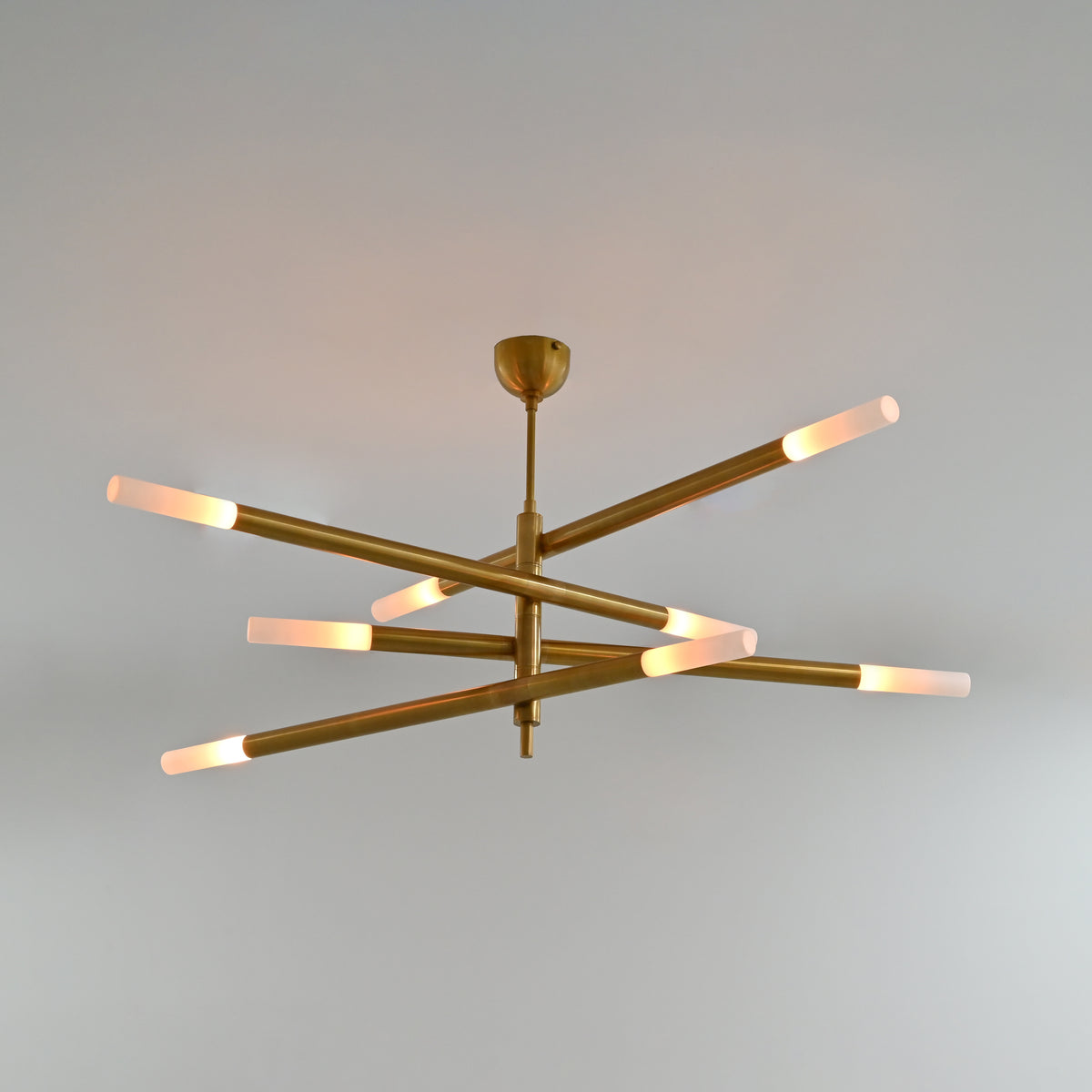 Marbella 8 light raw brass chandelier with four tubular arms, illuminated ends and modern linear ceiling design