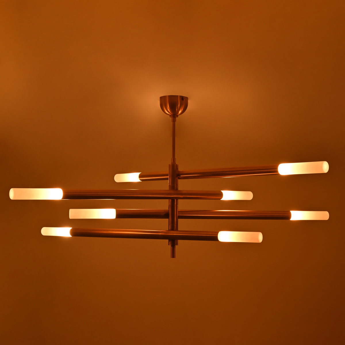 Illuminated Marbella brass chandelier with eight glowing tube ends and warm ambient light