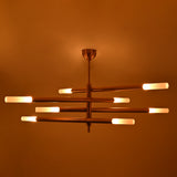 Illuminated Marbella brass chandelier with eight glowing tube ends and warm ambient light