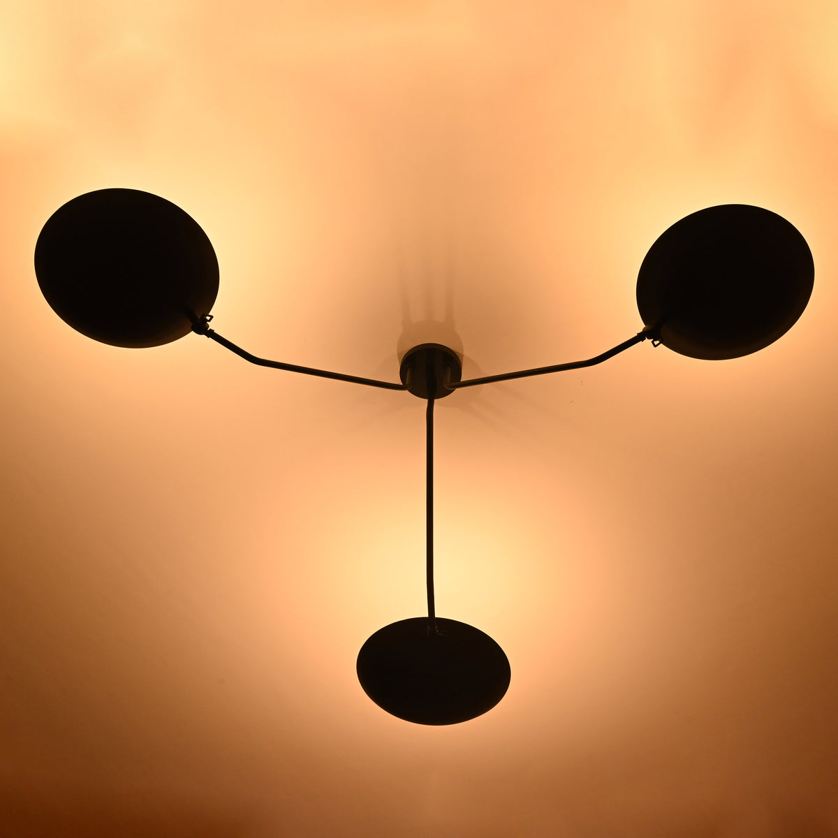 Illuminated view of matte black 3-light ceiling chandelier emitting soft, ambient golden lighting