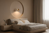 A minimalist wall sconce with a dark brown conical shade and a small green accent, mounted on a textured wall and casting a warm golden light into a large circular recess.