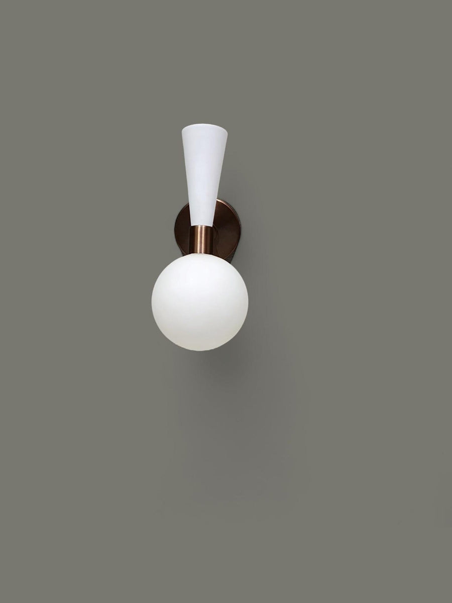 Two-tone brass and white wall sconce with frosted glass globe illuminated, handcrafted by Brass Leaf Studio