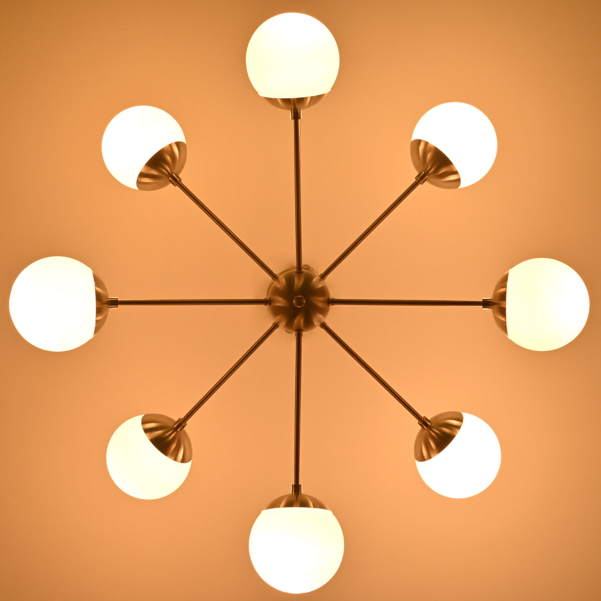 Overhead view of mid-century modern chandelier with brushed nickel arms and glowing white globe shades.