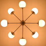 Overhead view of mid-century modern chandelier with brushed nickel arms and glowing white globe shades.