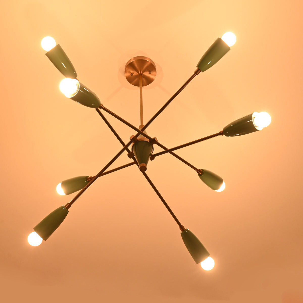 Mid-century style Sputnik chandelier with glowing warm light bulbs and teal cone-shaped shades, viewed from below against a softly lit ceiling