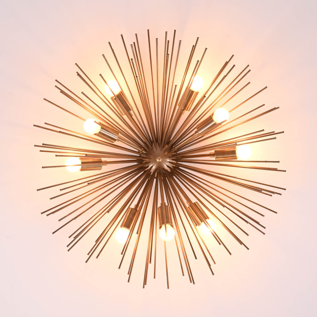 Top view of mid century starburst brass chandelier with radiant rods and warm glowing bulbs