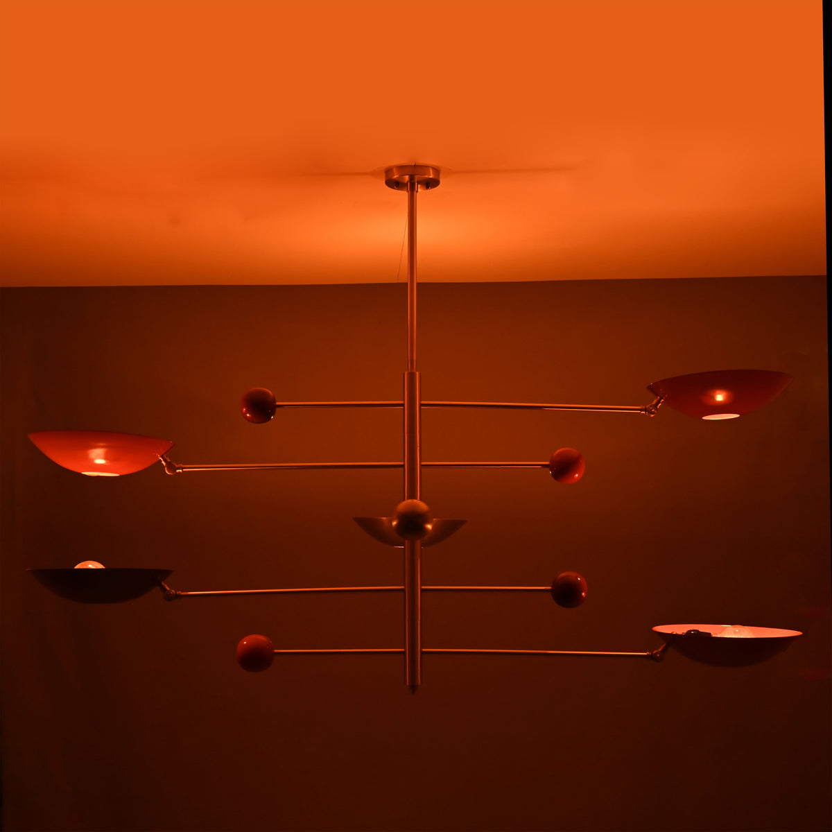 Mid-century modern mobile chandelier featuring brushed brass construction and red bowl shades arranged on balanced rods.