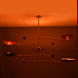 Mid-century modern mobile chandelier featuring brushed brass construction and red bowl shades arranged on balanced rods.