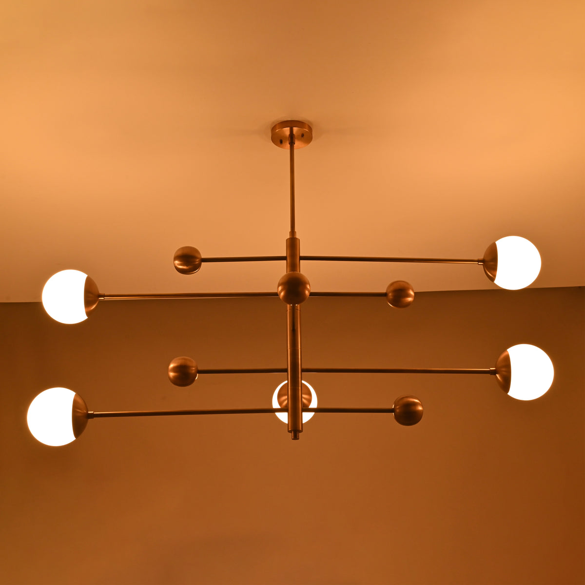 Night-lit view of minimalist 5-light brass chandelier with glowing white globes suspended on sleek horizontal arms.