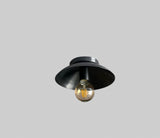 Wide view of minimalist blackened brass ceiling lamp showcasing elegant industrial design and warm glowing bulb.