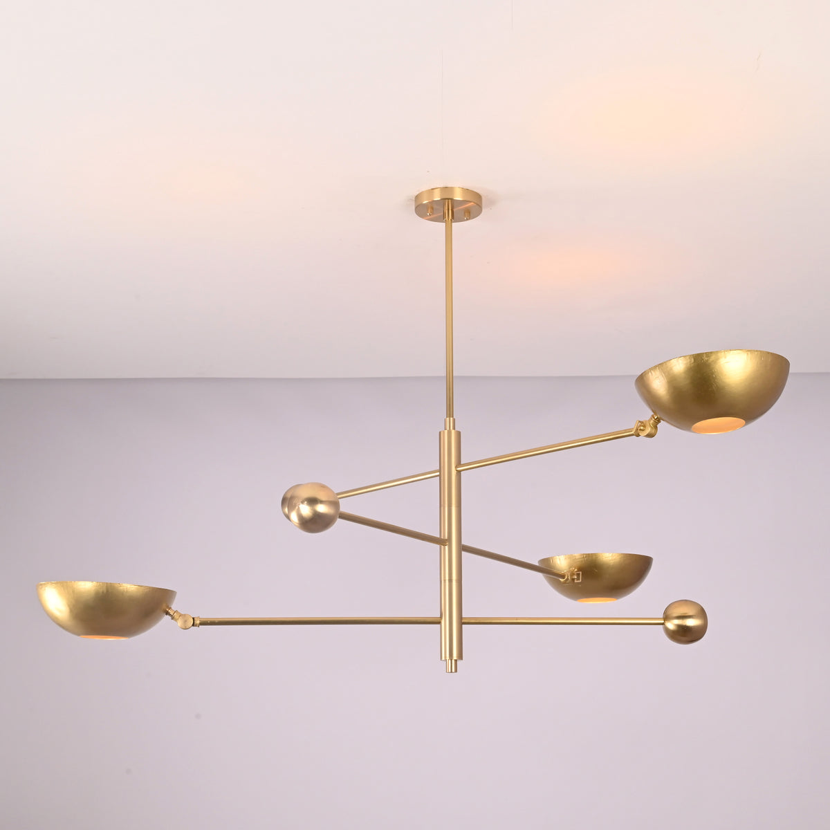 Angled view of minimalist brass disc chandelier showcasing sculptural arms and bowl shades