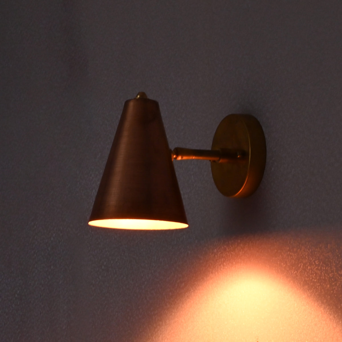 Minimalist brass wall light with copper cone shade glowing warmly in a dim setting