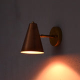 Minimalist brass wall light with copper cone shade glowing warmly in a dim setting