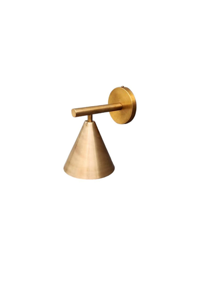 Minimalist brass cone wall light photographed on white background highlighting conical silhouette and handcrafted brass texture.