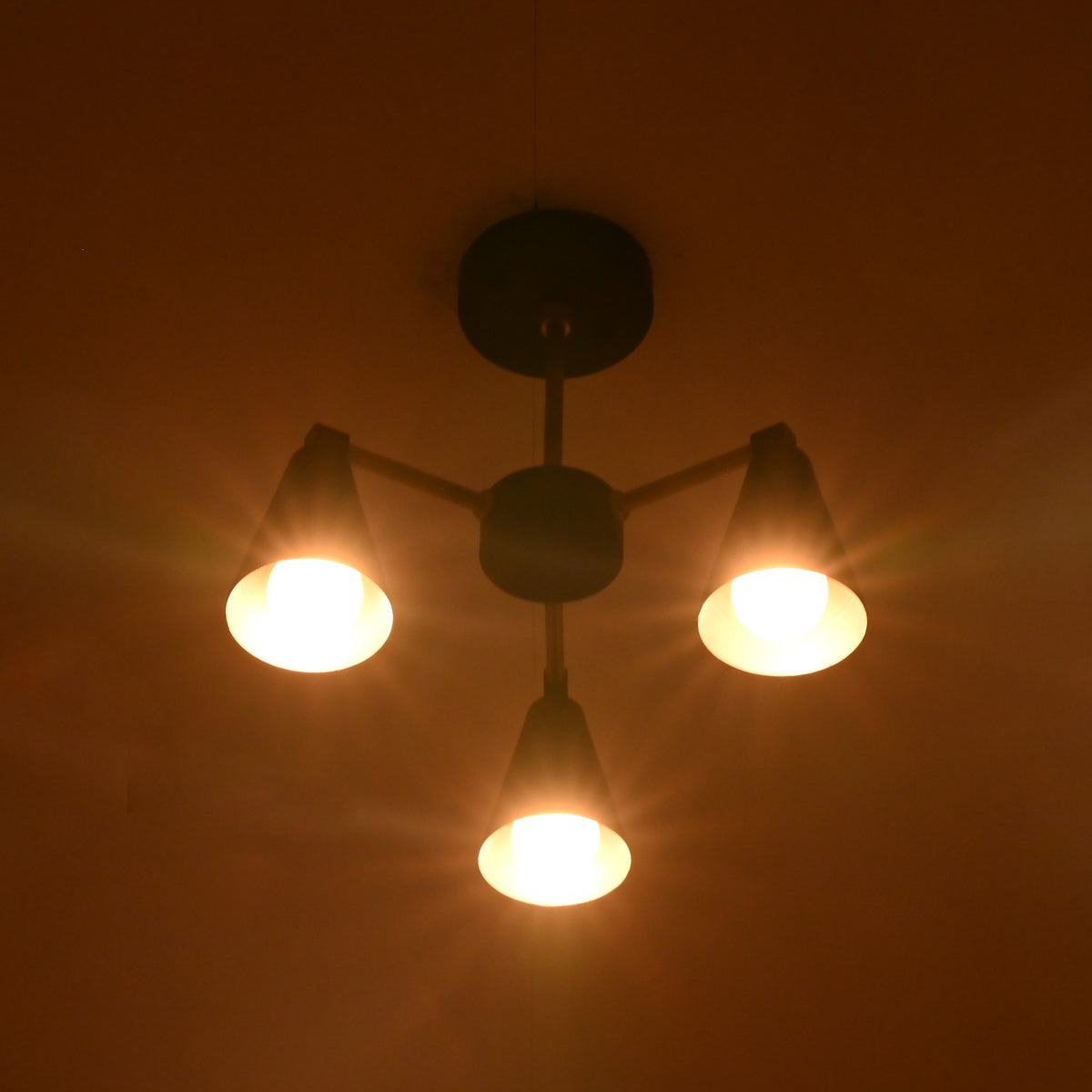 Bottom view of minimalist cone chandelier with three warm glowing lights