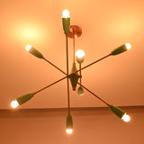 Angled dark room view of mint green 8 light brass chandelier with glowing bulbs and copper accents.