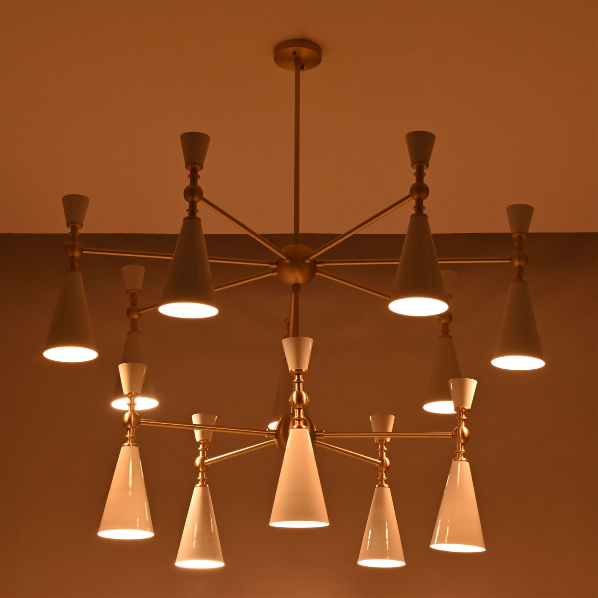Modern 12-light cone chandelier shown on white background with brushed brass structure and white enamel painted shades