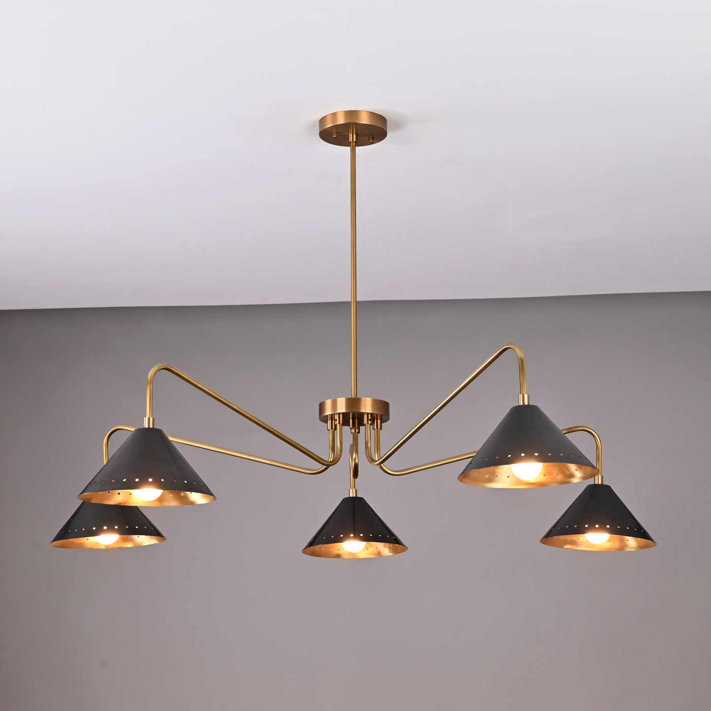 Front view of handcrafted 5-light brass chandelier featuring matte-black perforated cone shades and brushed brass arms.