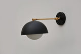 Modern black dome wall sconce featuring a white globe diffuser and brushed brass swing arm for warm ambient lighting.