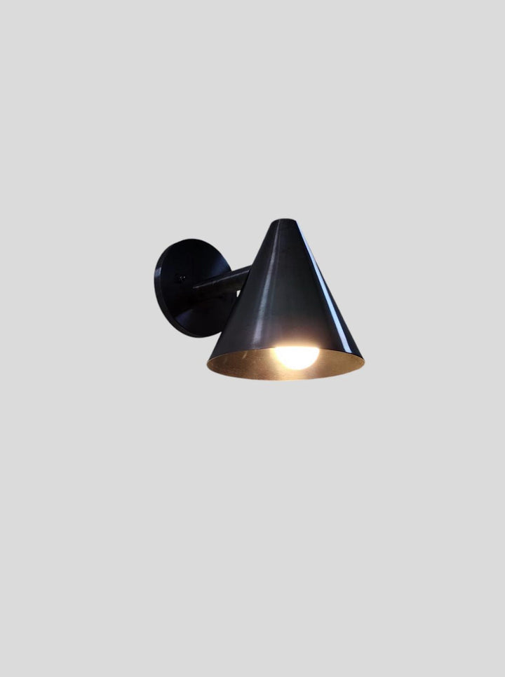 Sleek blackened brass wall sconce with illuminated cone shade, designed for modern and industrial interior lighting décor.