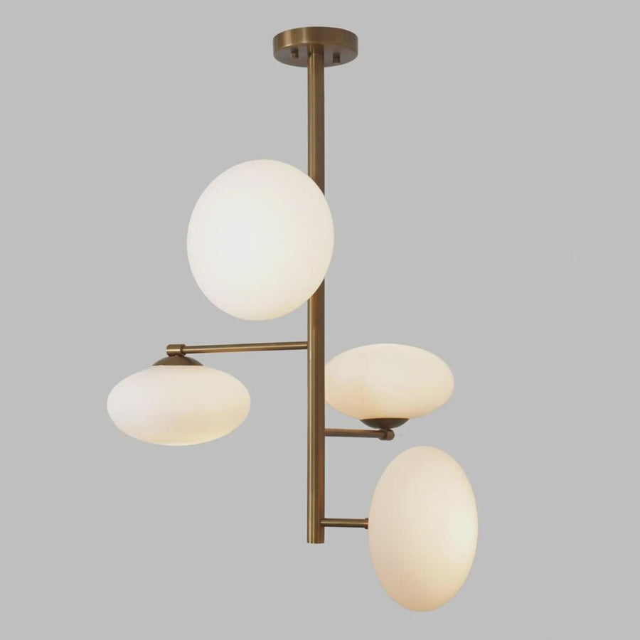 Modern 4-light brass chandelier with milky glass globe shades, featuring a vertical sculptural design and warm ambient lighting by Brass Leaf Studio.