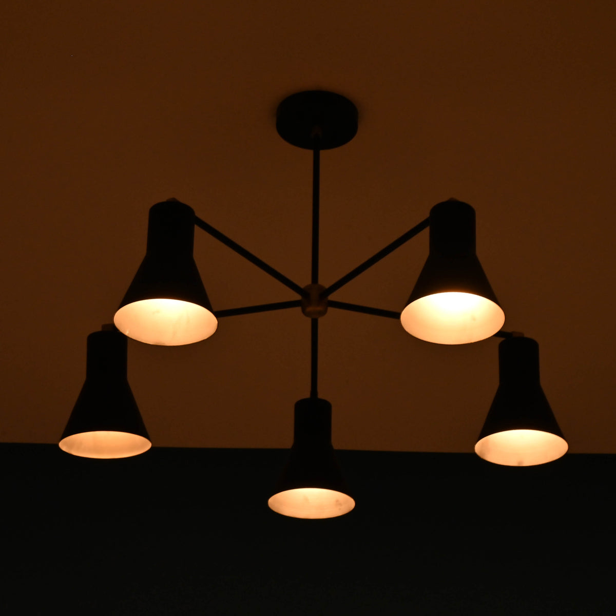 Modern brass 5 cone chandelier illuminated in dark room creating warm ambient lighting effect