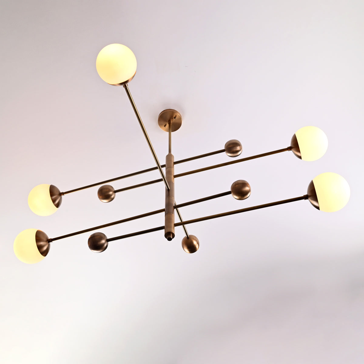 Side-angle view of a modern 5-light brass chandelier with round opal glass globes and minimalist brass arms.