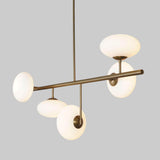 Modern 5-light brass chandelier with milky glass globe shades, featuring a sculptural linear design and warm ambient lighting by Brass Leaf Studio.