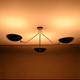 Modern brass-arm chandelier with three matte black bowl shades casting soft, warm ceiling illumination.