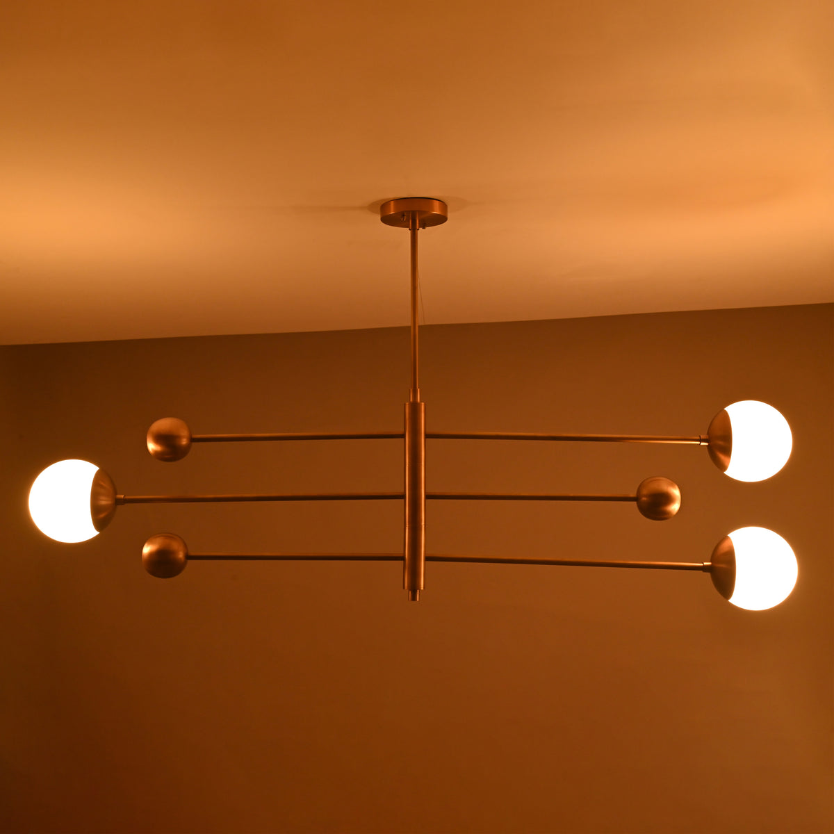 Warm-lit view of modern brass chandelier with three glowing opal globes, mid-century style lighting fixture.