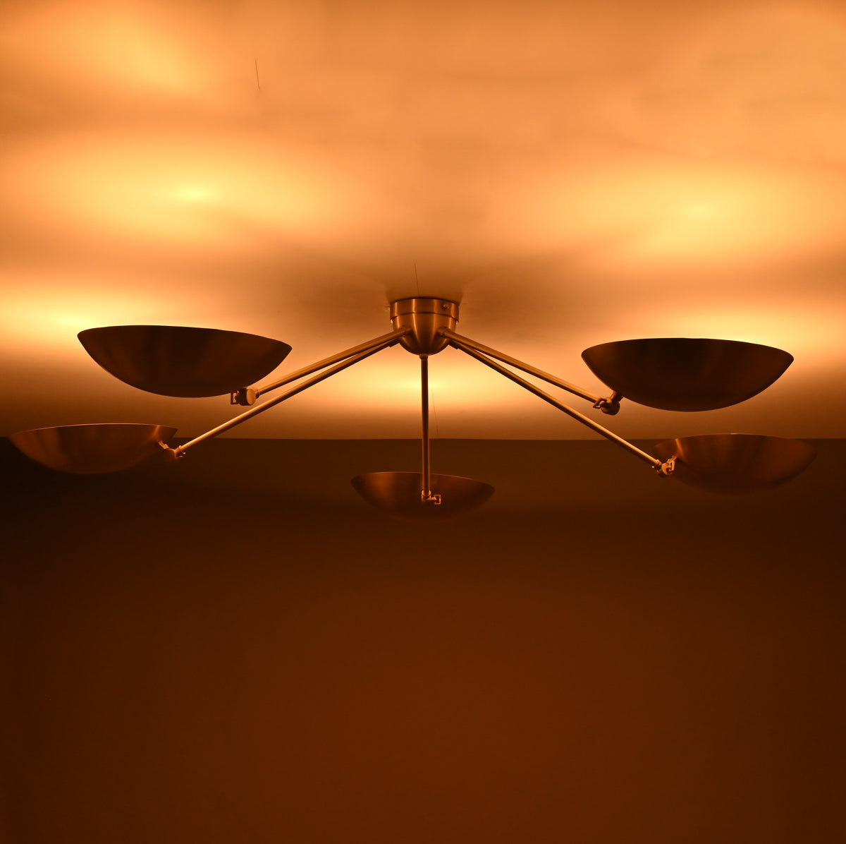 Modern brass ceiling light producing indirect upward glow through sculpted bowl-shaped shades.