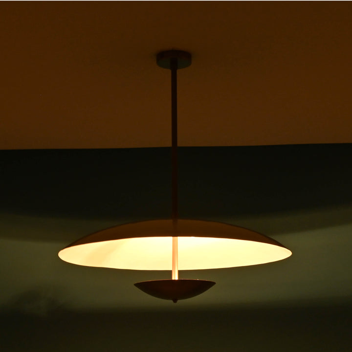 Modern brass ceiling light emitting a warm ambient glow, designed with a sleek dome silhouette, perfect for cozy dining or living areas.