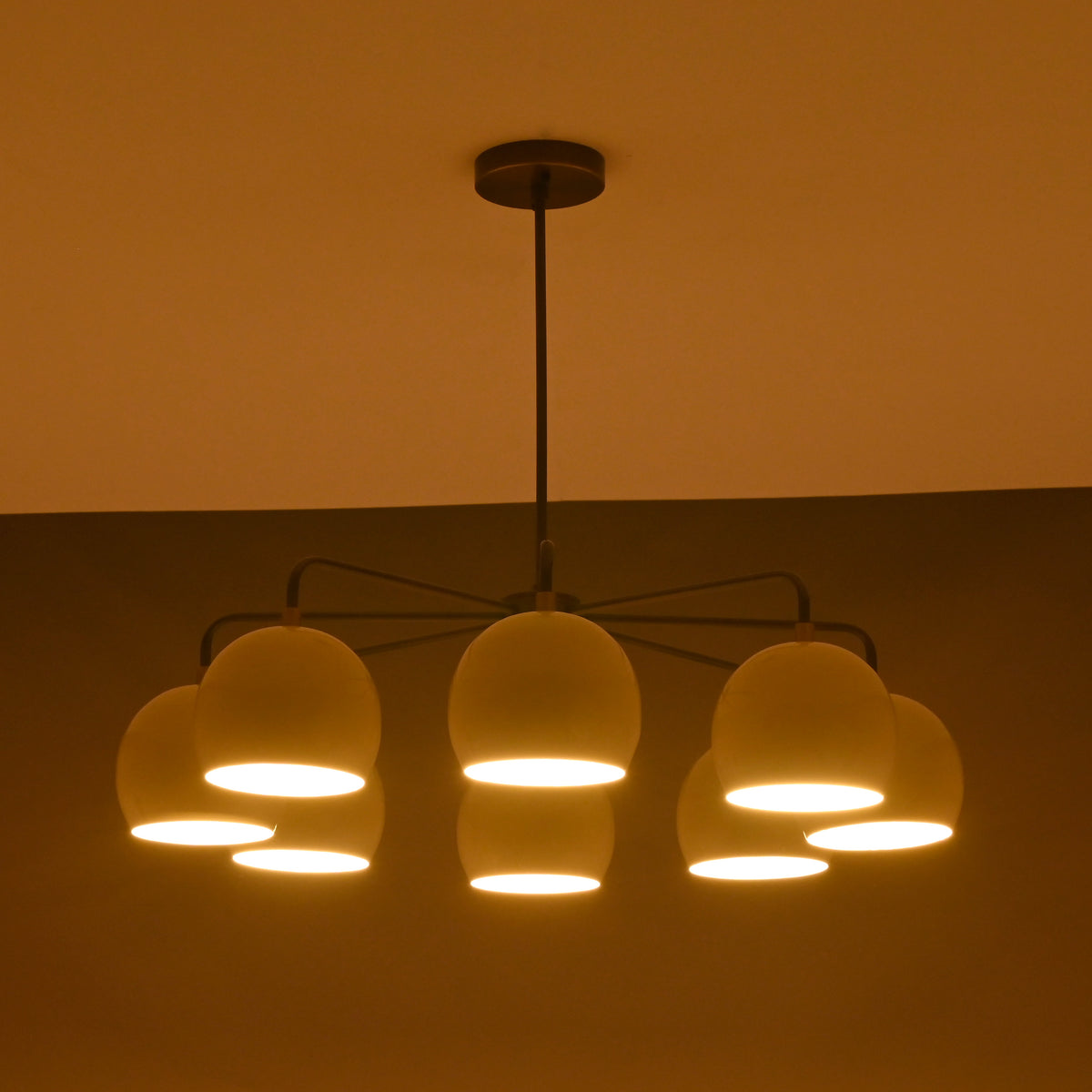 Minimalist 8-light chandelier in brass with soft evening light illuminating ivory dome shades.