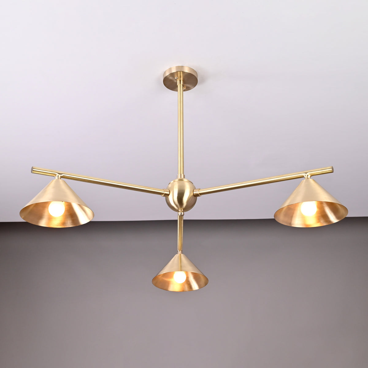 Close-up view of modern brushed brass chandelier with three cone-shaped shades, showcasing elegant handcrafted ceiling light design