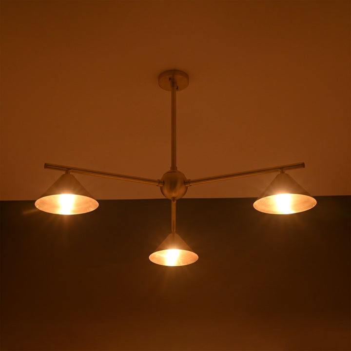 Brushed brass chandelier with three cone-shaped shades glowing in warm ambient light, ideal for cozy interior ceiling lighting
