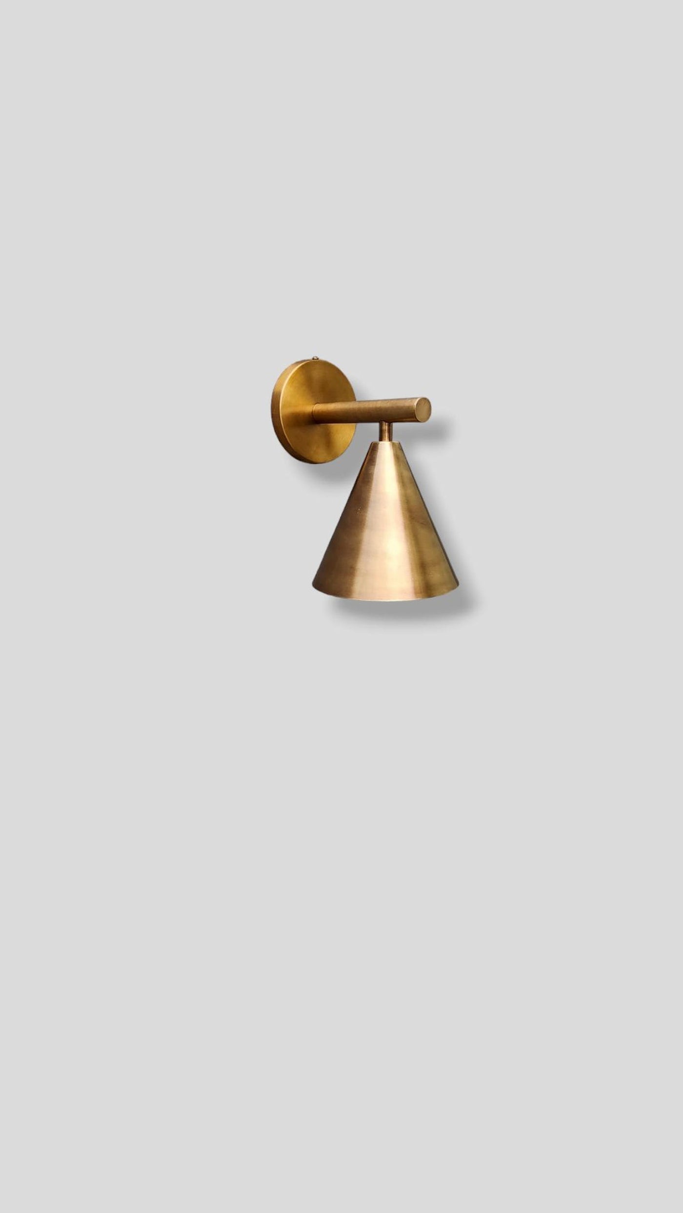 Side view of modern brass cone wall light handcrafted by Brass Leaf Studio in brushed raw brass finish, mounted on neutral background.