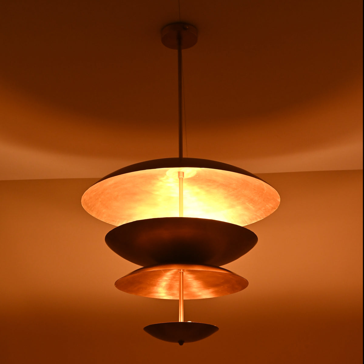 Modern brass disc chandelier glowing with warm ambient lighting and sculptural layered bowls.