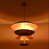 Modern brass disc chandelier glowing with warm ambient lighting and sculptural layered bowls.