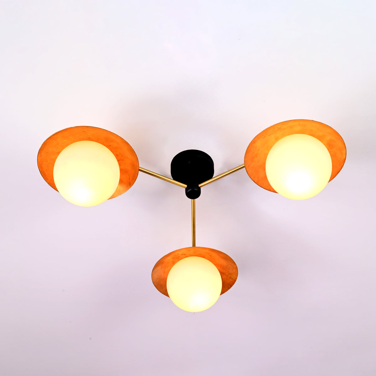 Modern brass disc ceiling light with three opal glass globes providing warm ambient illumination.
