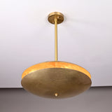 Modern brass disc pendant light viewed from a low upward angle, displaying warm inner glow and handcrafted hammered surface.