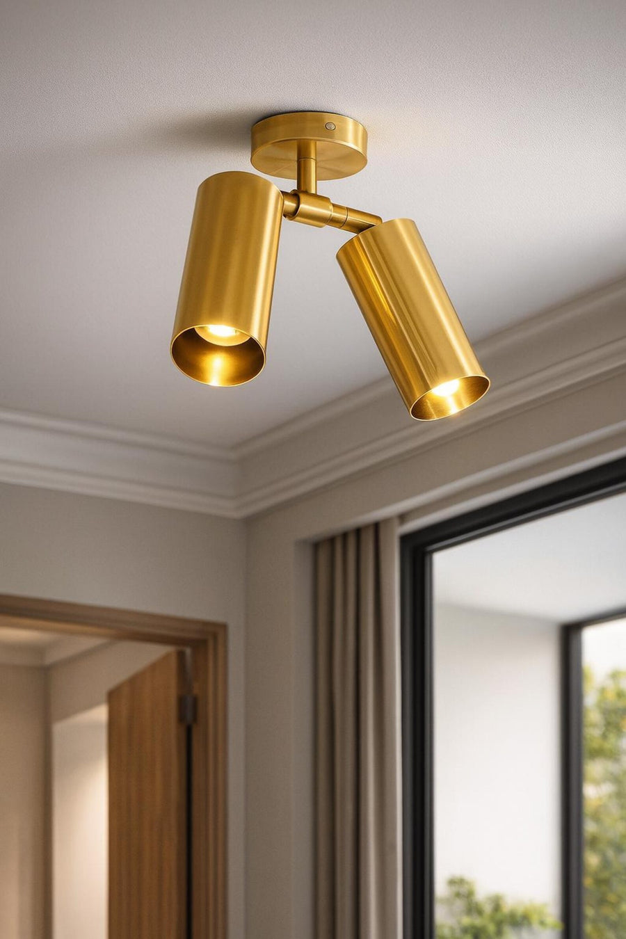 Modern brushed brass double cylinder ceiling spotlight with adjustable heads mounted on white ceiling in contemporary interior.