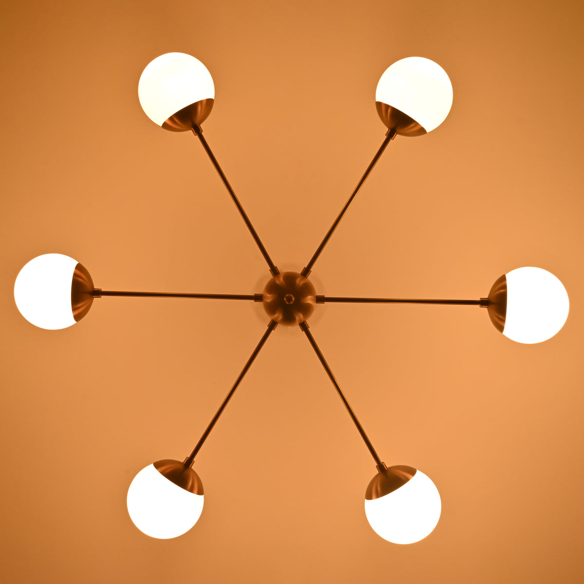 Warm-lit brass chandelier with six glowing globe shades creating a soft ambient atmosphere.
