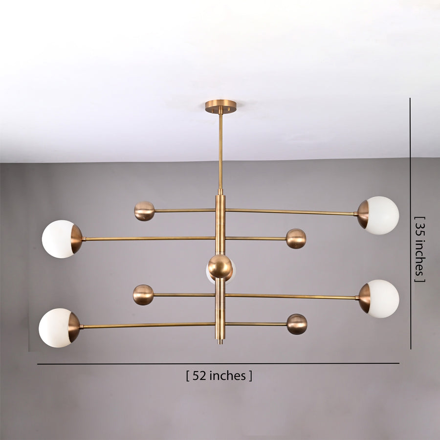 Brass linear chandelier creating warm lighting in a luxury bedroom interior with soft globe shades
